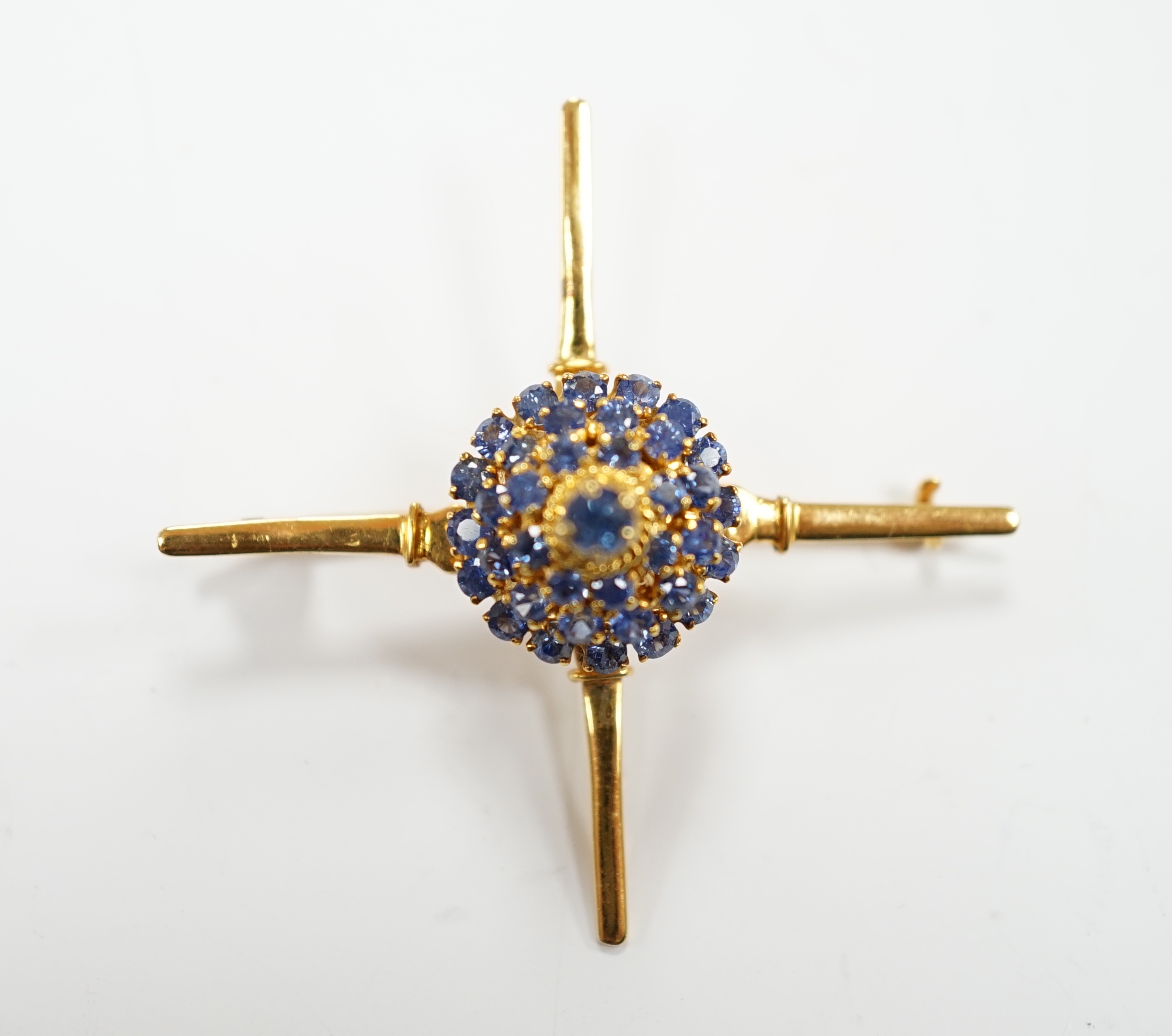 A yellow metal and sapphire cluster set brooch, of 'X' form with raised central motif, 45mm, gross weight 6.2 grams.